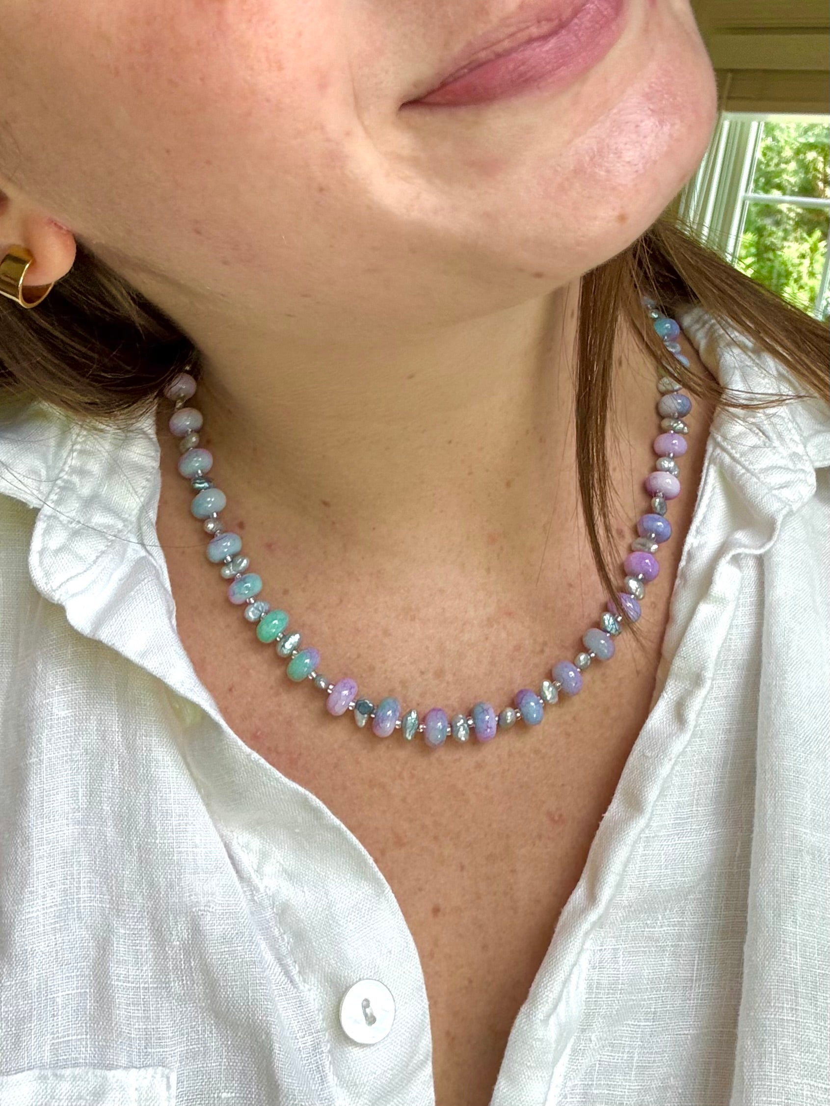 Person wearing a beaded necklace with a white shirt, outdoors.